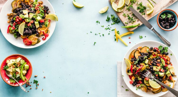 Colorful Mexican salad with avocado, black beans, and lime on a light blue surface.