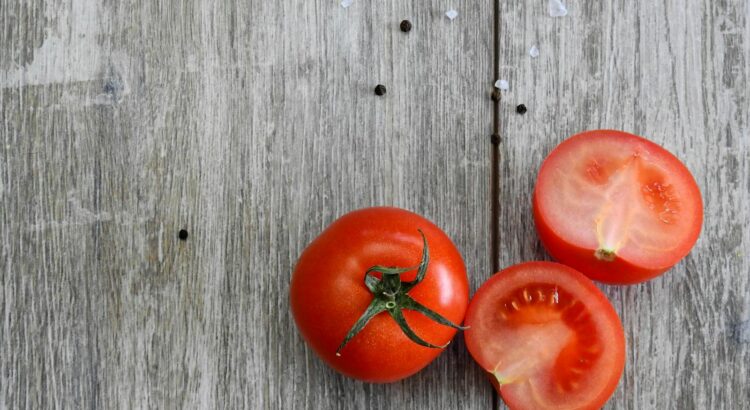 Close-up of ripe tomatoes on a rustic wooden table with peppercorns.
